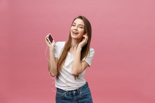 Lifestyle Concept. Young woman using phone for listening to music on pink background.