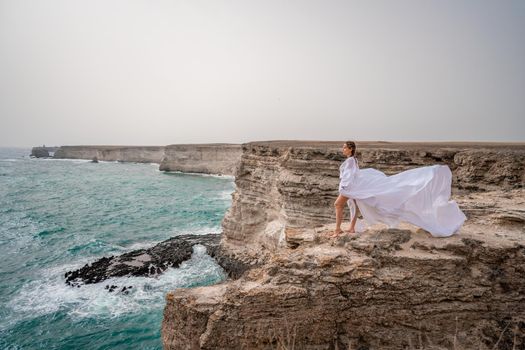 Happy freedom woman on the beach enjoying and posing in white dress over the sea. View of a girl in a fluttering white dress in the wind. Holidays, holidays at sea