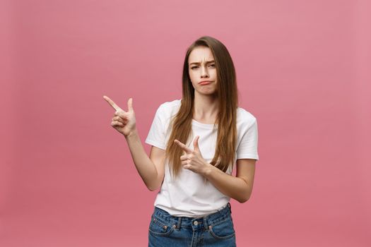 Closeup of serious strict young woman wears white shirt looks stressed and pointing up with finger isolated over pink background.