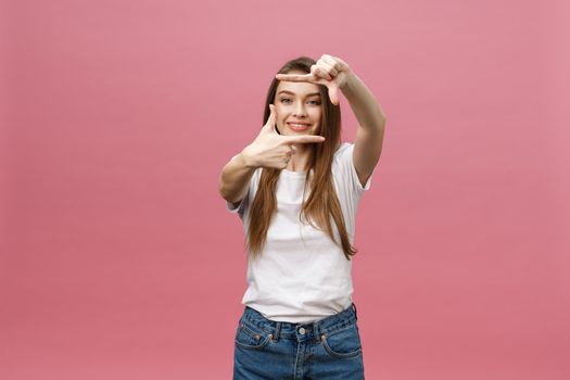 Cheerful young woman keeping mouth wide open, looking surprised, making hands photo frame gesture isolated on bright pink background