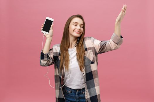 Lifestyle Concept. Young woman using phone for listening to music on pink background.