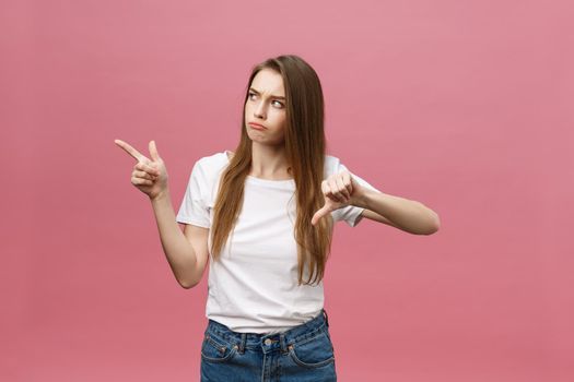 Closeup of serious strict young woman wears white shirt looks stressed and pointing up with finger isolated over pink background.