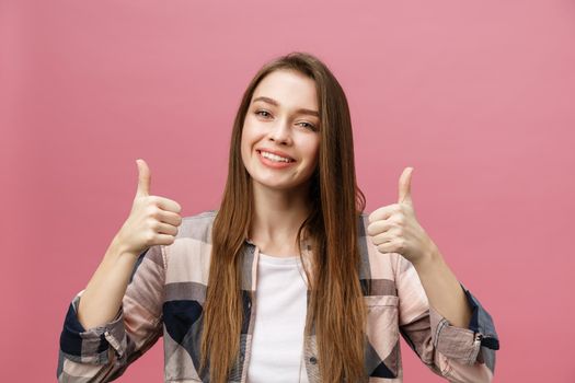 Close-up shot of smiling pretty girl showing thumb up gesture. Female isolated over pink background in the studio