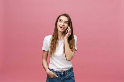 Cheerful young woman talking on mobile phone isolated on pink background.