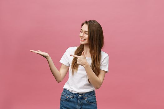 young girl with white shirt pointing hand on side to present a product on isolated pink background.