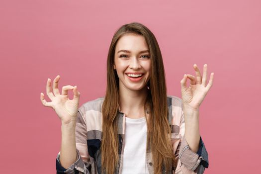 Attractive young adult woman showing ok sign. Expression emotion and feelings concept. Studio shot, isolated on pink background