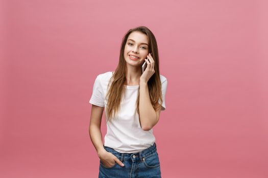 Cheerful young woman talking on mobile phone isolated on pink background.