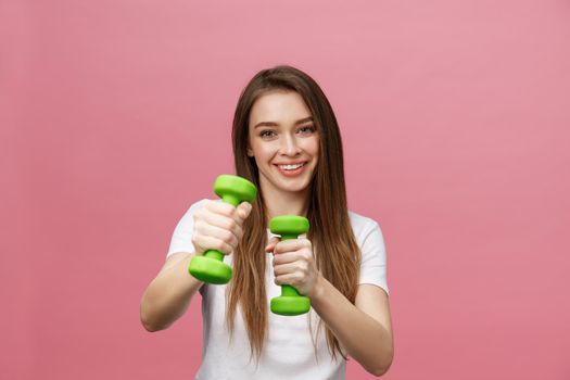 Fitness, young woman with dumbbells at studio background. Pretty girl isolate over pink.