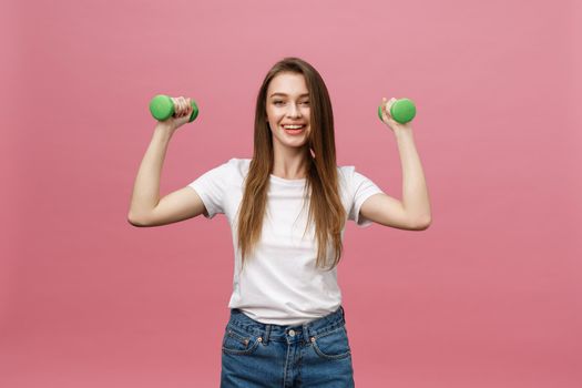 Fitness, young woman with dumbbells at studio background. Pretty girl isolate over pink.