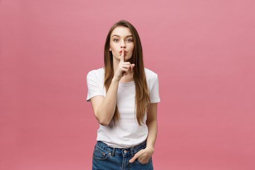 Portrait of young woman with finger on lips against pink wall.