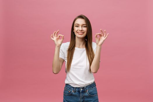 Attractive young adult woman showing ok sign. Expression emotion and feelings concept. Studio shot, isolated on pink background