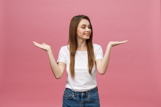 young girl with white shirt pointing hand on side to present a product on isolated pink background.