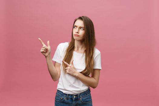 Closeup of serious strict young woman wears white shirt looks stressed and pointing up with finger isolated over pink background.