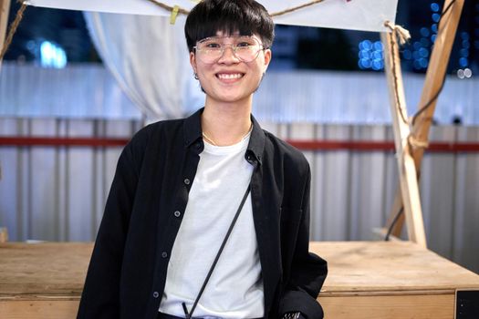 Portrait of a non-binary person with glasses standing in a night fair in the city of Bangkok