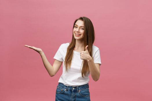 Close-up shot of smiling pretty girl showing thumb up gesture. Female isolated over pink background in the studio