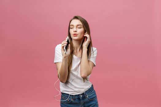 Lifestyle Concept. Young woman using phone for listening to music on pink background.