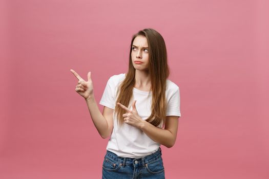 Closeup of serious strict young woman wears white shirt looks stressed and pointing up with finger isolated over pink background.