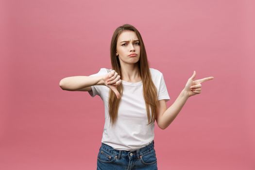Closeup of serious strict young woman wears white shirt looks stressed and pointing up with finger isolated over pink background.