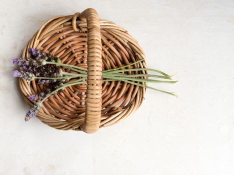 Top down view of small bunch of lavender in wicker basket on neutral limestone background (selective focus)