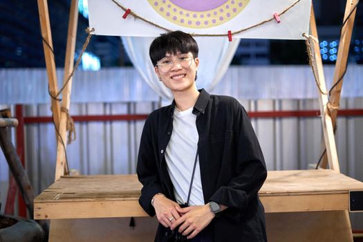 Portrait of a non-binary person with glasses smiling to the camera in an urban night fair