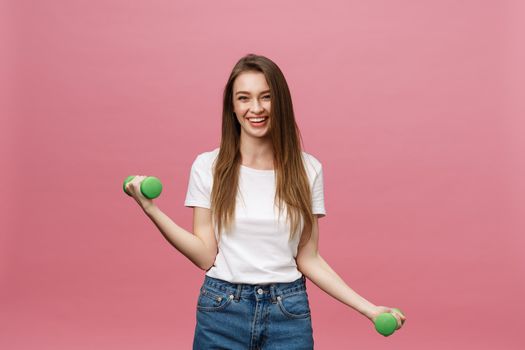 Fitness, young woman with dumbbells at studio background. Pretty girl isolate over pink.