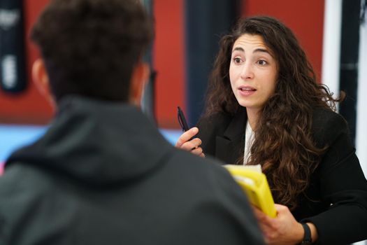 Female sports psychologist with pen and folder speaking with male athlete during motivational session in contemporary gym