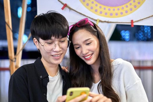 portrait of a lesbian couple looking at a mobile phone in the middle of a night fair in Thailand