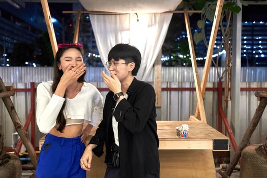 Two lesbian women covering their mouth while laughing in a counter of a stall in a night fair