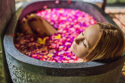 Attractive Young woman in bath with petals of tropical flowers and aroma oils. Spa treatments for skin rejuvenation. Alluring woman in Spa salon. Girl relaxing in bathtub with flower petals. Luxury.