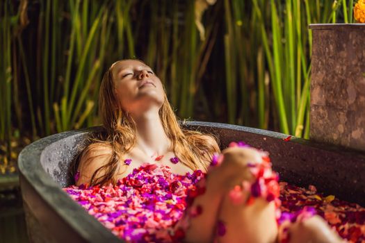 Attractive Young woman in bath with petals of tropical flowers and aroma oils. Spa treatments for skin rejuvenation. Alluring woman in Spa salon. Girl relaxing in bathtub with flower petals. Luxury.