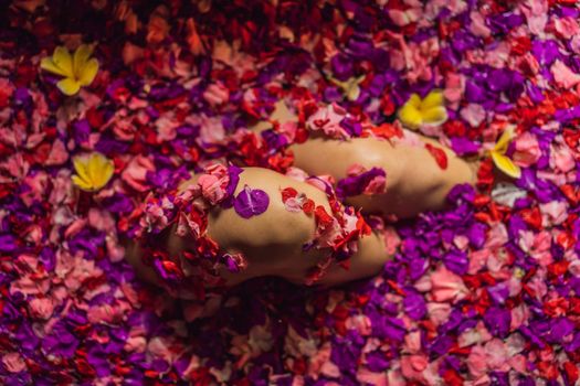 Attractive Young woman in bath with petals of tropical flowers and aroma oils. Spa treatments for skin rejuvenation. Alluring woman in Spa salon. Girl relaxing in bathtub with flower petals. Luxury.