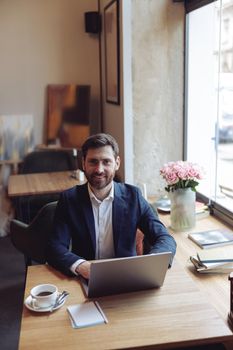 Caucasian handsome man smiling, sitting at table with laptop in cafe. Business. Vertical. Portrait.
