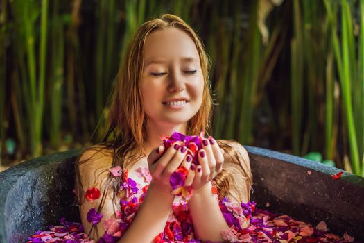 Attractive Young woman in bath with petals of tropical flowers and aroma oils. Spa treatments for skin rejuvenation. Alluring woman in Spa salon. Girl relaxing in bathtub with flower petals. Luxury.