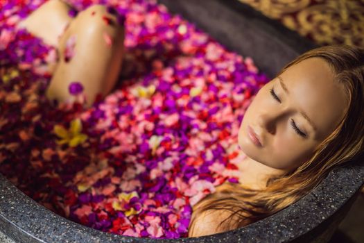 Attractive Young woman in bath with petals of tropical flowers and aroma oils. Spa treatments for skin rejuvenation. Alluring woman in Spa salon. Girl relaxing in bathtub with flower petals. Luxury.