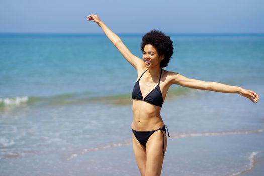 Happy African American woman opening her arms on the beach to enjoy her holiday in the sun.