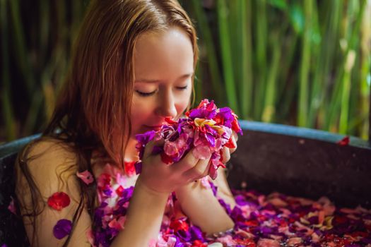 Attractive Young woman in bath with petals of tropical flowers and aroma oils. Spa treatments for skin rejuvenation. Alluring woman in Spa salon. Girl relaxing in bathtub with flower petals. Luxury.