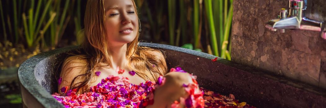 Attractive Young woman in bath with petals of tropical flowers and aroma oils. Spa treatments for skin rejuvenation. Alluring woman in Spa salon. Girl relaxing in bathtub with flower petals. Luxury. BANNER, LONG FORMAT