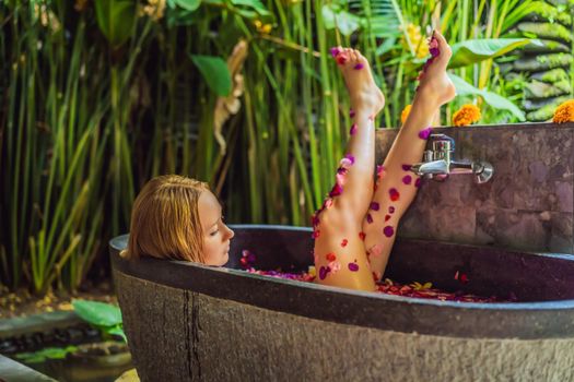 Attractive Young woman in bath with petals of tropical flowers and aroma oils. Spa treatments for skin rejuvenation. Alluring woman in Spa salon. Girl relaxing in bathtub with flower petals. Luxury.