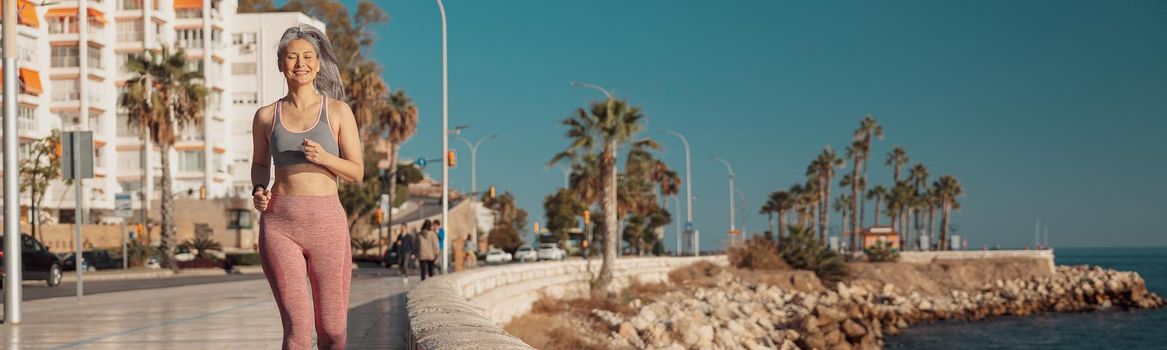 Smiling woman in sports top and pink leggings training on the seashore and looking ahead on warm sunny day