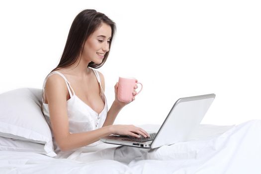 Smiling woman catching up on her social media as she relaxes in bed with a laptop computer