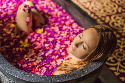 Attractive Young woman in bath with petals of tropical flowers and aroma oils. Spa treatments for skin rejuvenation. Alluring woman in Spa salon. Girl relaxing in bathtub with flower petals. Luxury.