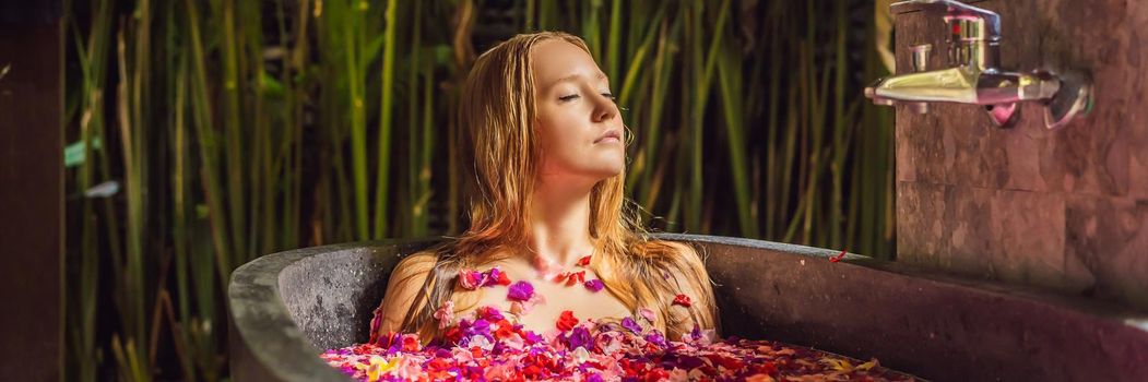 Attractive Young woman in bath with petals of tropical flowers and aroma oils. Spa treatments for skin rejuvenation. Alluring woman in Spa salon. Girl relaxing in bathtub with flower petals. Luxury. BANNER, LONG FORMAT