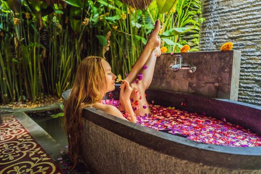 Attractive Young woman in bath with petals of tropical flowers and aroma oils. Spa treatments for skin rejuvenation. Alluring woman in Spa salon. Girl relaxing in bathtub with flower petals. Luxury.