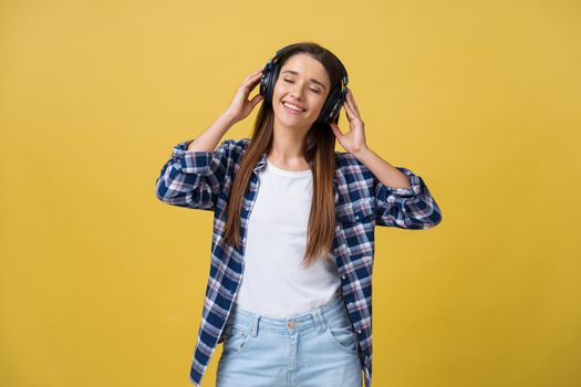 Beautiful calm young woman listening the music in headphone with closed eyes on yellow background. Closeup.