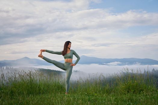 Fitness young lady in sport clothes stretching legs during morning time among foggy mountains. Concept of people, activity and workout.