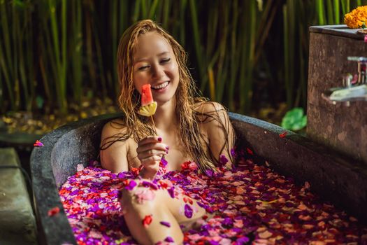 Attractive Young woman in bath with petals of tropical flowers and aroma oils. Spa treatments for skin rejuvenation. Alluring woman in Spa salon. Girl relaxing in bathtub with flower petals. Luxury.