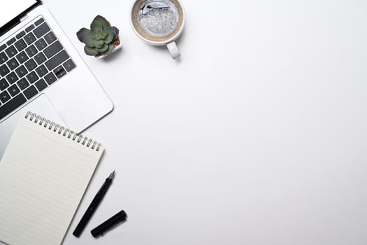 Minimal workplace with laptop computer, coffee cup, blank notepad and succulent plant. Top view with copy space.