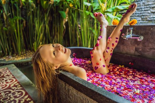 Attractive Young woman in bath with petals of tropical flowers and aroma oils. Spa treatments for skin rejuvenation. Alluring woman in Spa salon. Girl relaxing in bathtub with flower petals. Luxury.