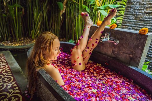 Attractive Young woman in bath with petals of tropical flowers and aroma oils. Spa treatments for skin rejuvenation. Alluring woman in Spa salon. Girl relaxing in bathtub with flower petals. Luxury.