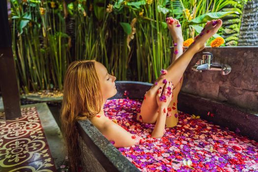 Attractive Young woman in bath with petals of tropical flowers and aroma oils. Spa treatments for skin rejuvenation. Alluring woman in Spa salon. Girl relaxing in bathtub with flower petals. Luxury.